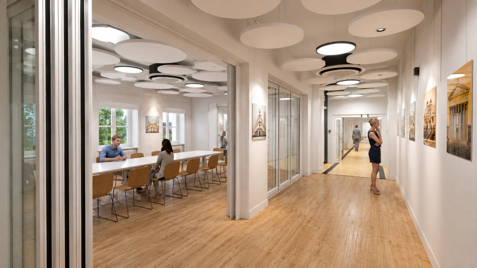Corridor with pale oak flooring, a sparser field of panels, a glazed meeting room to the left and building prints along the right-hand wall