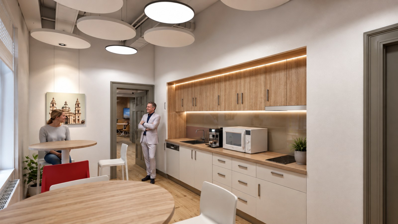 Tea point with an oak run of cabinets, concealed lighting, round standing tables, floating panels overhead and exposed ductwork
