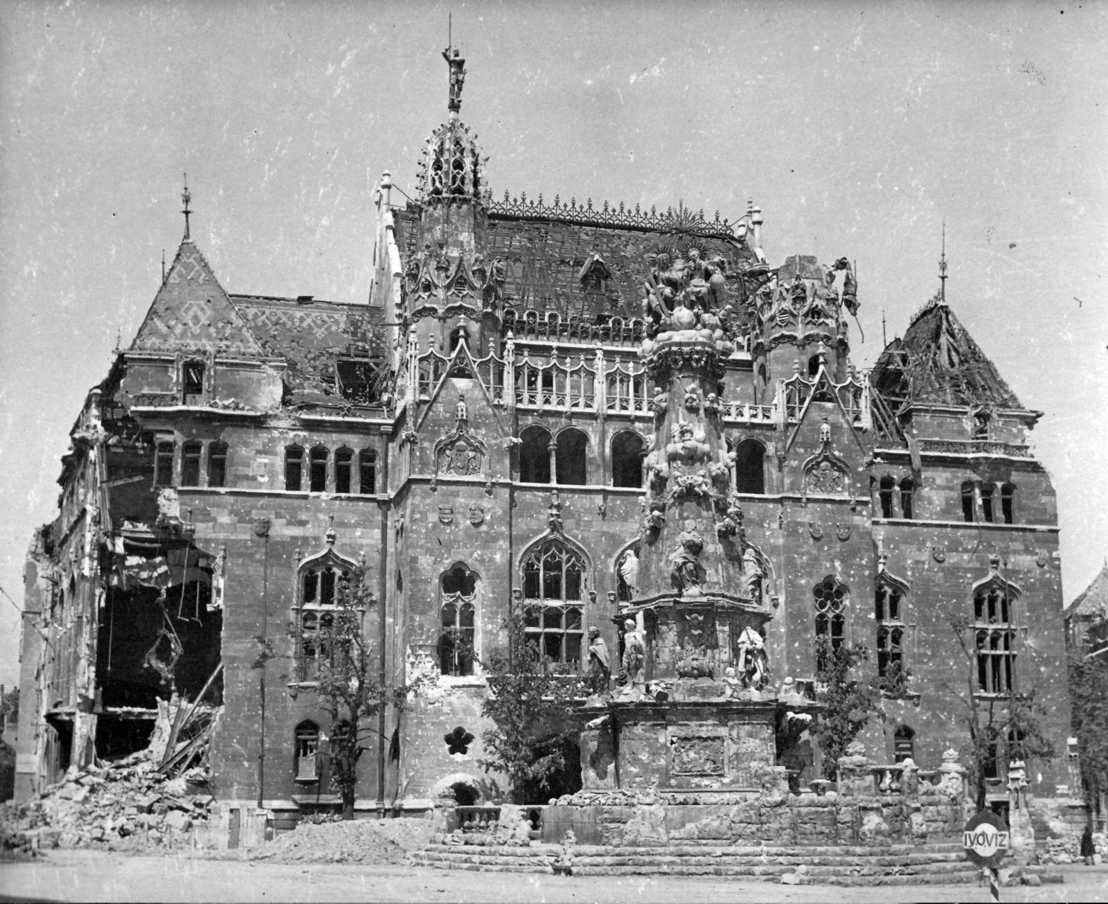 Archive black-and-white photograph of the palace burned out in the war: roof lost, facade damaged, rubble around the Holy Trinity column