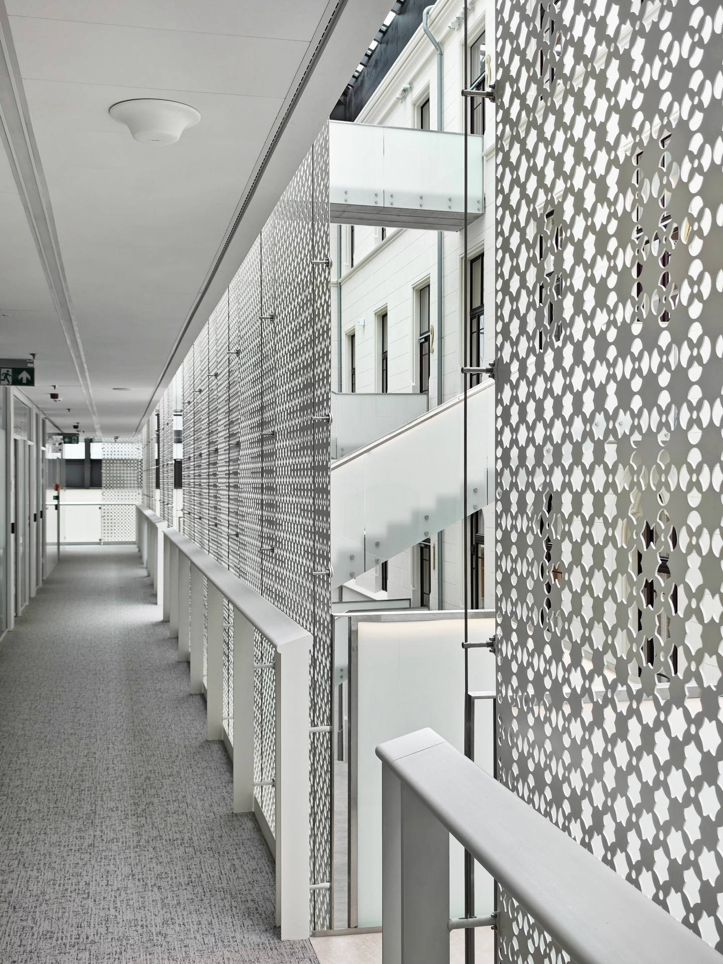 Corridor along the perforated metal wall: the tracery pattern of the panel close up, the restored facade behind it