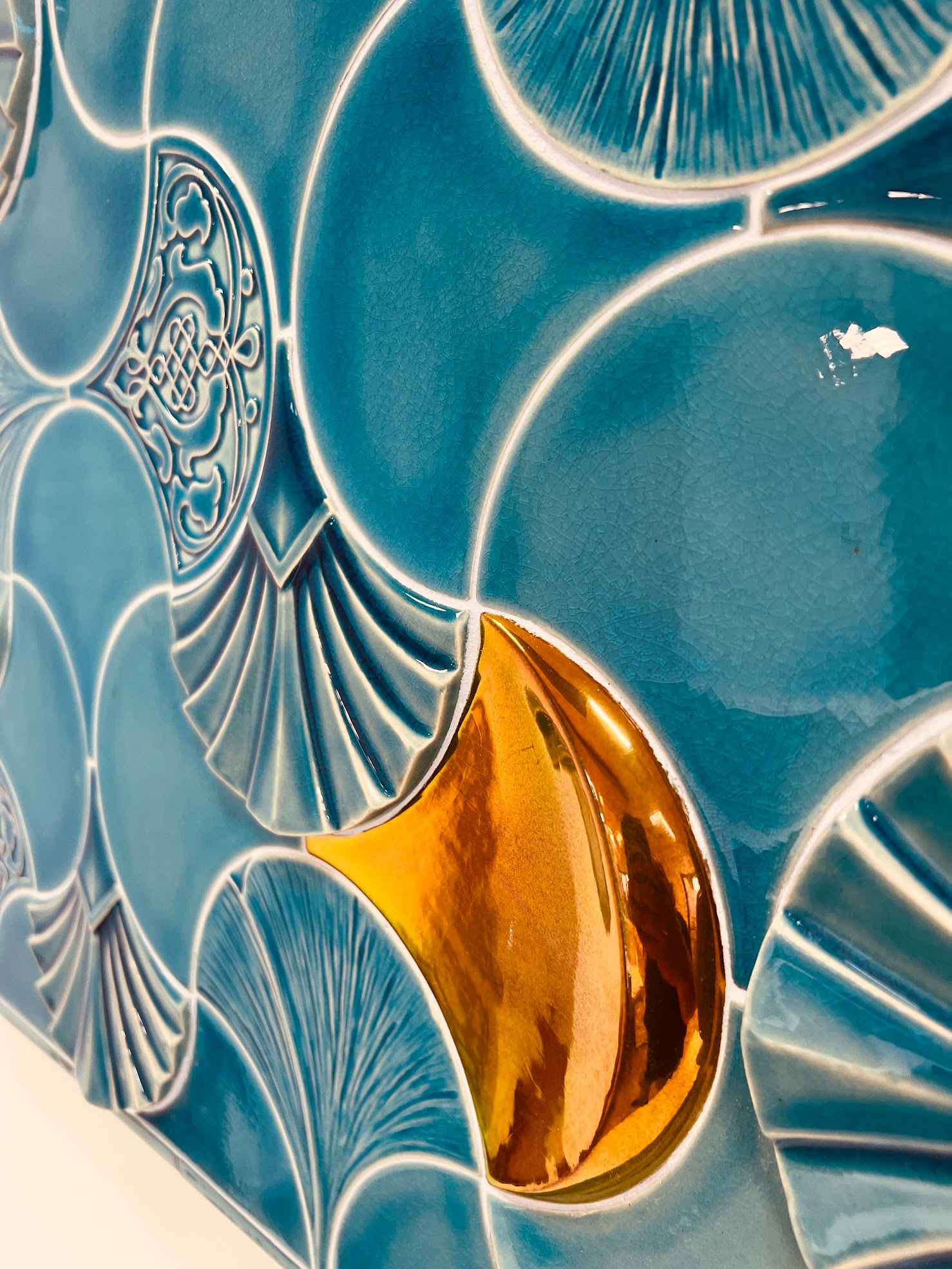 Close view of the ceramic wall: a gold-lustre ginkgo leaf among celadon-glazed relief elements