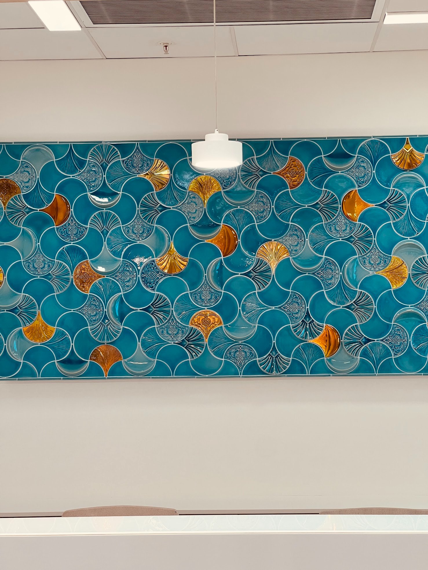 A celadon-glazed relief ceramic wall with gold-lustre ginkgo motifs on an office reception wall
