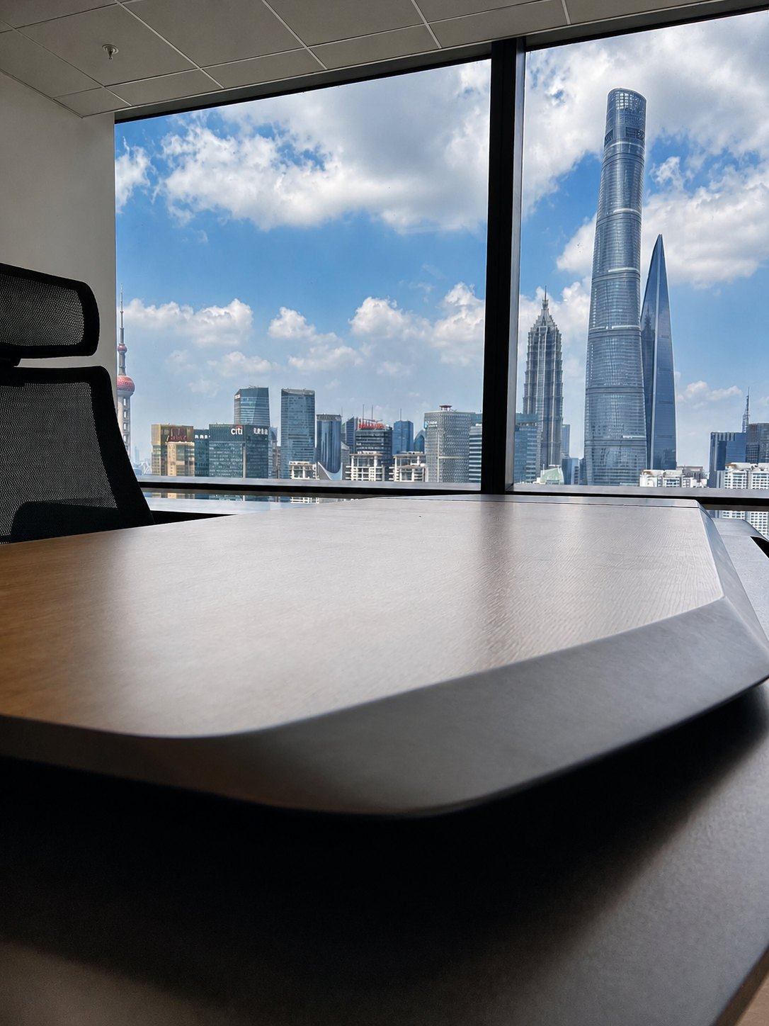 The corner of a meeting table in front of the façade glazing, with the Pudong towers beyond