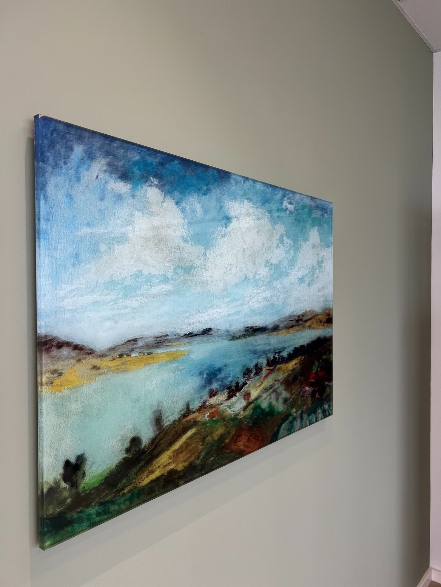 A painting carried onto glass: a Danube Bend landscape with blue sky and clouds, on a sand-coloured wall