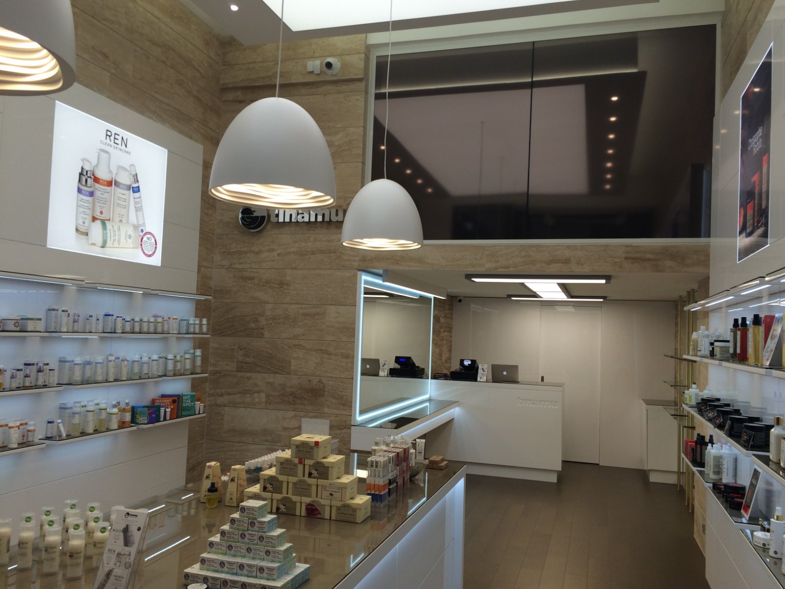 Make-up counter with a lit-frame mirror under the mezzanine, the till behind, a travertine band on the wall