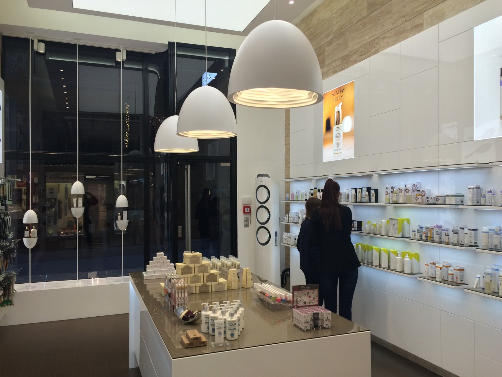 The shop by day: three large white pendants above the island counter, customers at the shelf wall