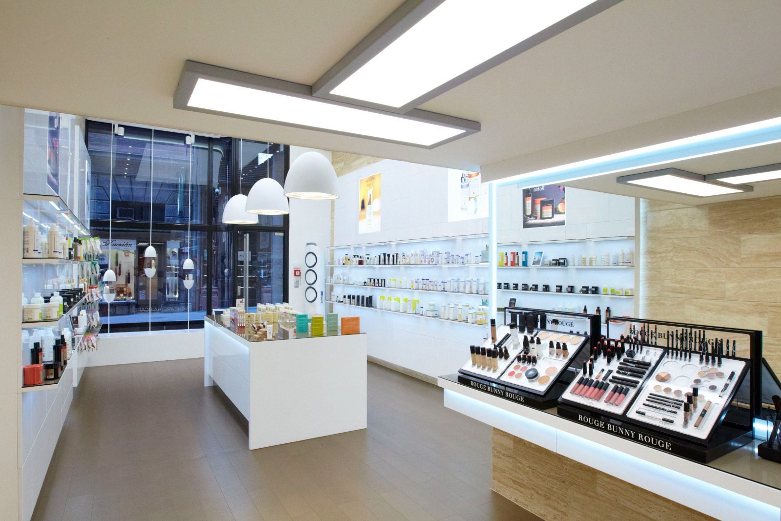 Interior of a cosmetics shop: a white island counter, backlit shelves, a mezzanine clad in travertine to the right